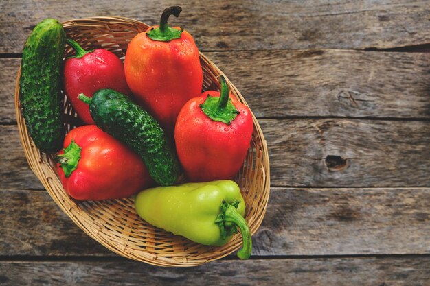 Paprika's en komkommers in een rieten mand op een rustieke houten tafel.