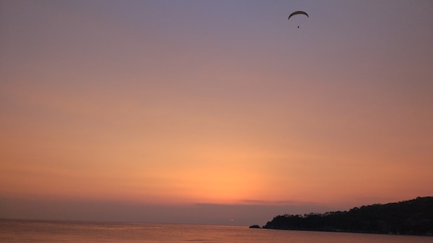 パラグライダーが夕日を背景に飛ぶ