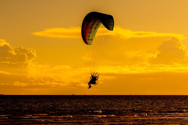 写真 海の上の夕日を背景にパラグライダーが飛ぶ