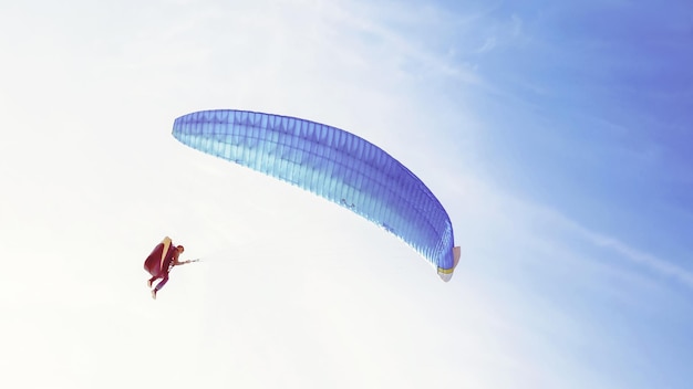 Paraglider met blauwe vleugel die in blauwe lucht vliegt