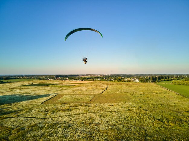 Photo paraglider soaring high above lush green fields on a sunny day