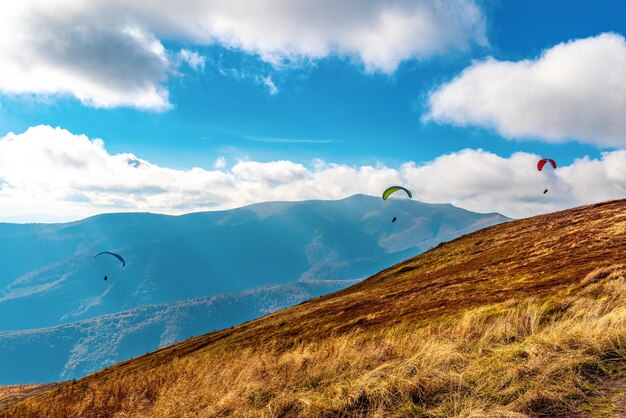 Paragliding actieve sporten met parachute vliegen tegen bergen met weelderige bossen in hoogland verlicht door zonlicht onder bewolkte hemel