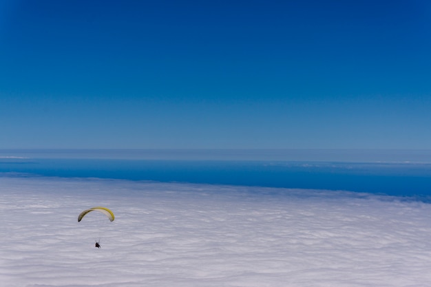 Paragliding over a sea of clouds in the sky in a clear sunny day