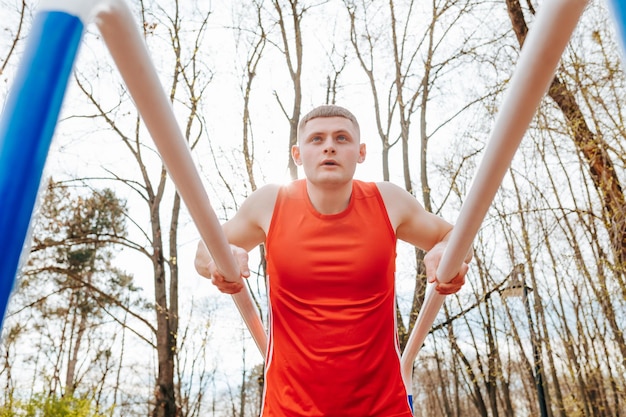 Foto parallel bars perfection il viaggio di allenamento di un giovane atleta questo ragazzo atletico sta mostrando le sue abilità sulle barre parallele durante la sua sessione di allenamento all'aperto indossando una maglietta rosso brillante