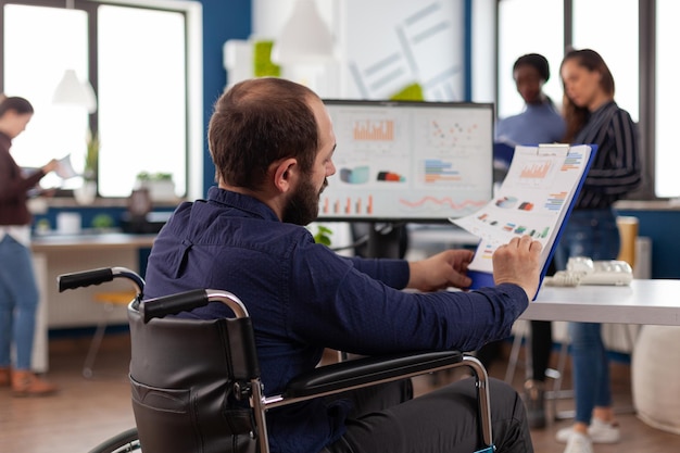 Paralyzed businessman analyzing financial graphs on clipboard in startup business office. Disabled executive manage working at management strategy planning company presentation