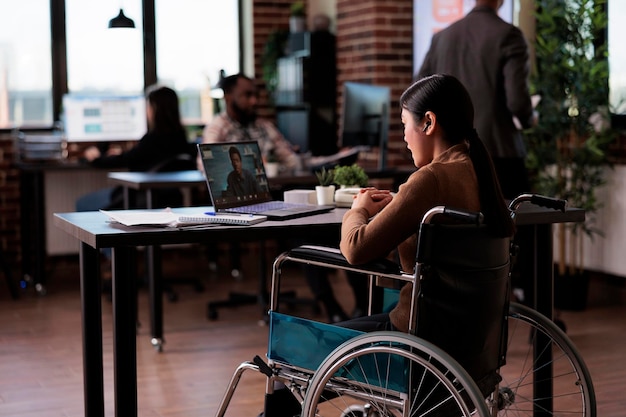 Paralyzed woman with impairment using remote teleconference\
chat on laptop, sitting in wheelchair. female employee with\
disability meeting on online videoconference call, telework.