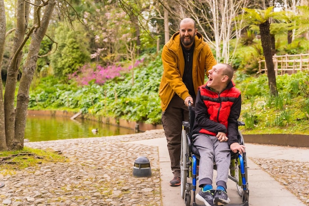 Paralyzed young man in a wheelchair being pushed by a friend in a public city park