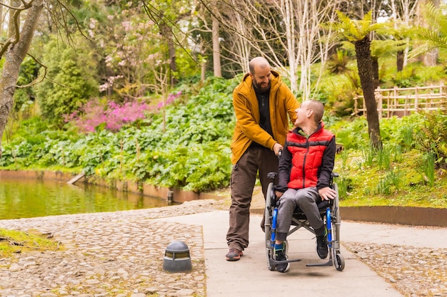 Paralyzed young man in a wheelchair being pushed by a friend in a public city park