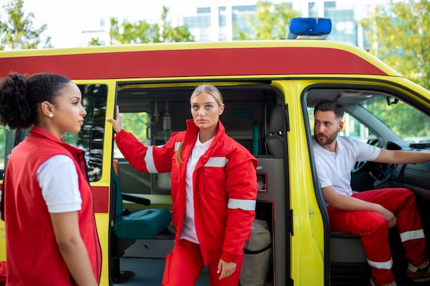 Paramedics and doctor standing on the side ambulance Doctor is carrying a medical trauma bag Group of three paramedics standing in front of ambulance with smile