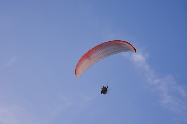 Парамотор (Powered Paraglider) с красно-белым парашютом, летящим в небе, экстремальный спорт.