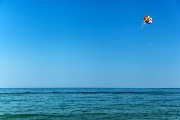 parasailing over the sea, sea, sky, activity, blue, parachute, people, summer, water, travel, entertainment, outdoor, tropical air, wind, extreme, flying with a parachute behind a boat, person, sport,