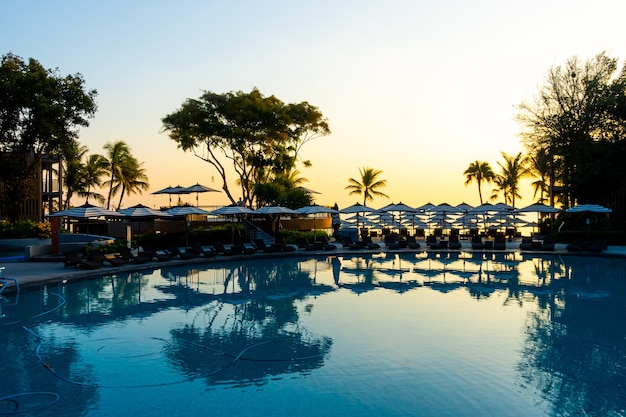 Parasol en stoelbank rond buitenzwembad in hotelresort voor vakantievakantie met zonsondergang of zonsopganghemel