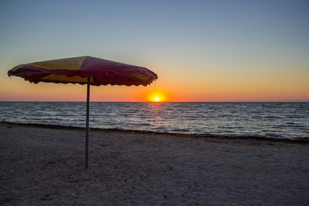 Parasol on seaside in sunrise with colorful sky on the horizon.