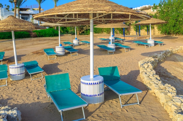 Parasols en lege ligstoelen op het zandstrand aan de kust