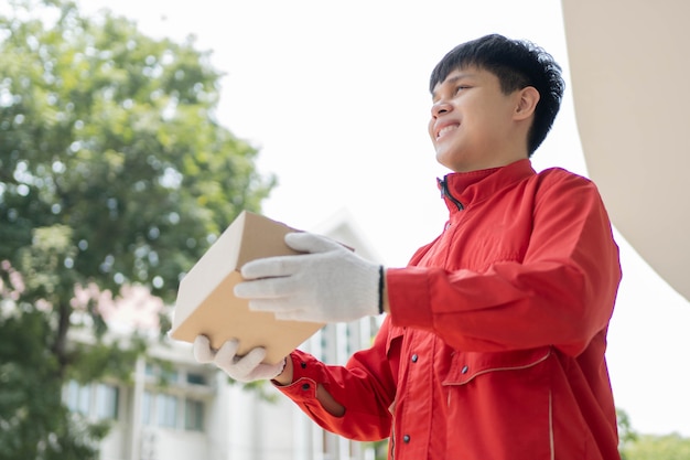 Концепция доставки посылок: почтальон в красной униформе и перчатках от некоторых логистических компаний передает посылку клиенту во время пандемии Covid19.