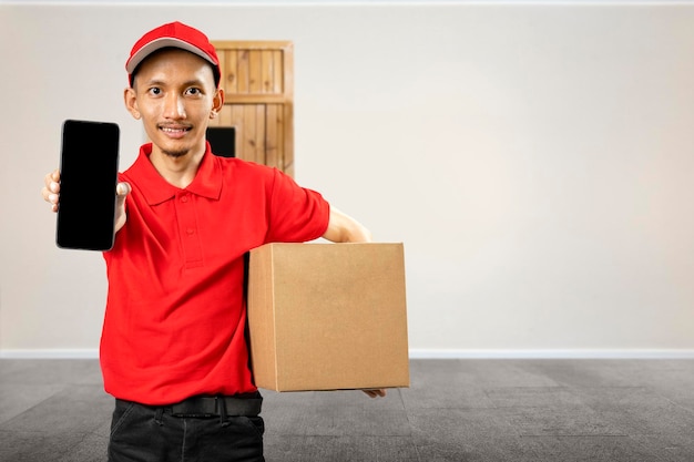 Parcel delivery man with a hat showing his mobile phone screen while carrying a package