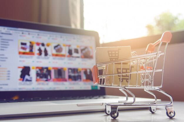 Parcel or Paper cartons with a shopping cart logo in a trolley on a laptop keyboard.