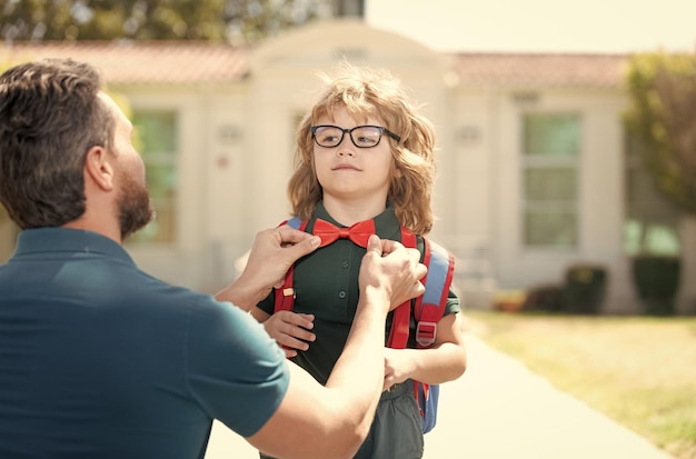 Parent gathering little child boy at first grade fix bow tie school