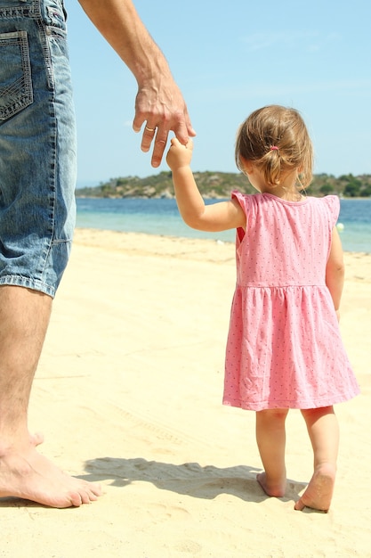 The parent holds the hand of a small child near the sea