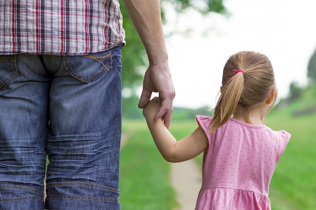 Родитель держит за руку маленького ребенка и гуляет