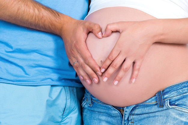 부모의 사랑과 행복한 모성. 임신 배의 배경에 심장 모양의 근접 촬영.