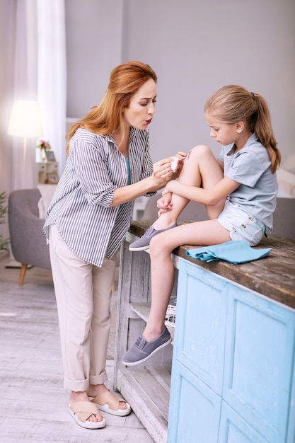 Parental love. Pleasant caring woman looking after her daughter while blowing at her wound