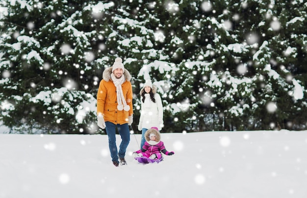親子関係、ファッション、季節、人のコンセプト – 冬の森をそりで歩く子どもと幸せな家族
