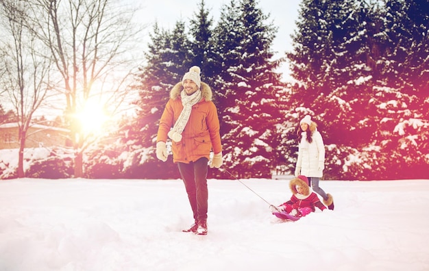 parenthood, fashion, season and people concept - happy family with child on sled walking in winter outdoors