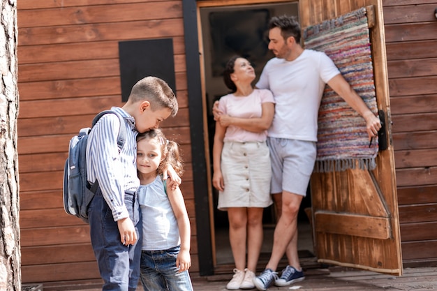 Foto i genitori sono felici di riportare i loro due figli a scuola e di finire felicemente l'apprendimento a distanza a casa, accompagnando i loro figli in piedi sulla soglia della loro casa