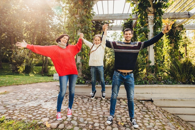 Parents and children concept Happy family have fun outdoors female and male play with little kid swing her in hands make gestures have wonderful relationship enjoy fresh autumn air