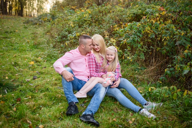 parents and daughter are sitting on the grass.