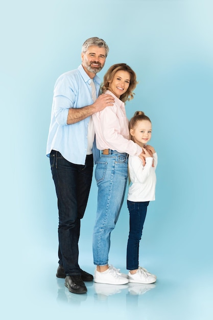 Parents and daughter embracing standing together over blue background vertical