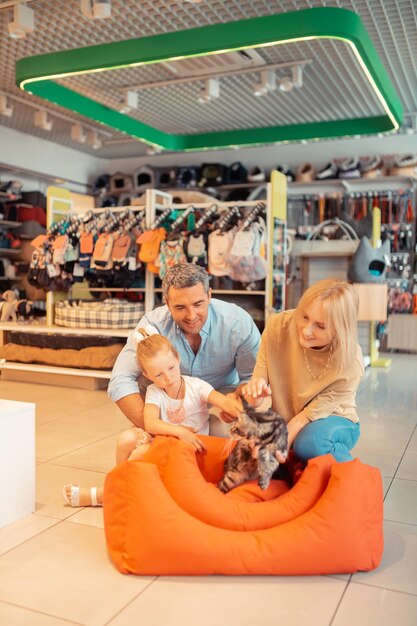 Parents and daughter playing with cat while visiting pet shop