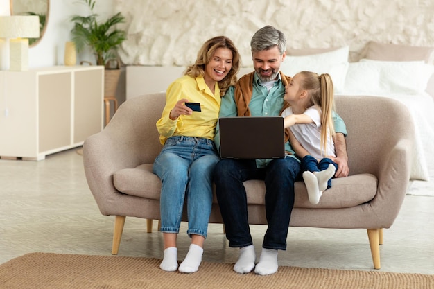 Parents and daughter shopping using credit card and laptop indoor