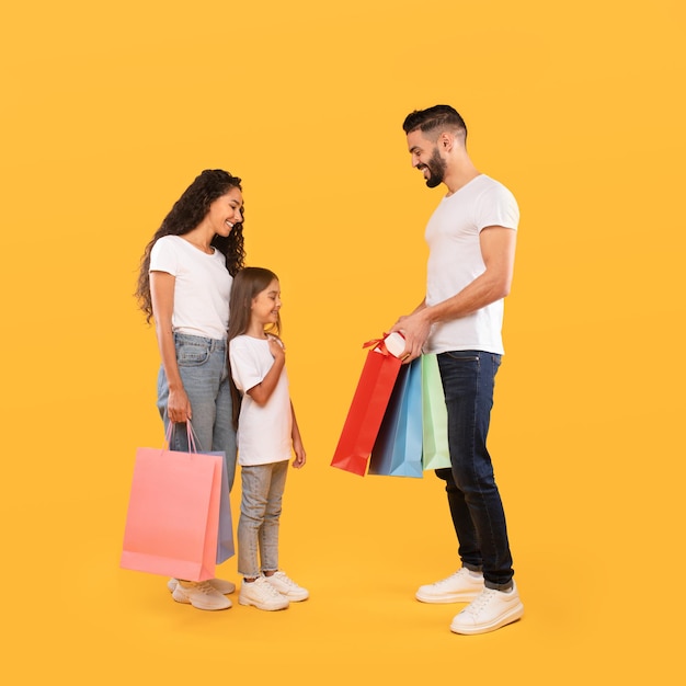 Parents giving gift and shopping bags to daughter yellow background