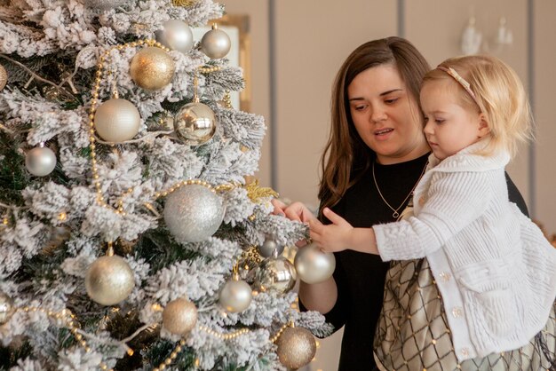 親と小さな娘がおもちゃと花束でクリスマスツリーを飾っています