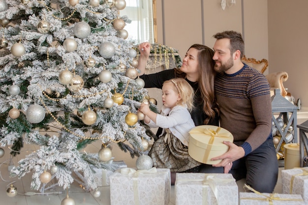 Parents and his little daughter decorating Christmas tree with toys and garlands