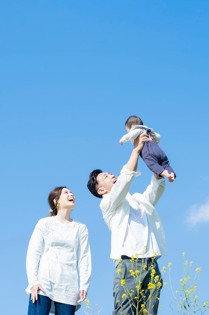 青い空の下で赤ちゃんを高く抱きしめる両親