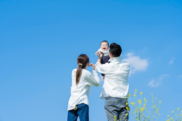 青い空の下で赤ちゃんを高く抱きしめる両親