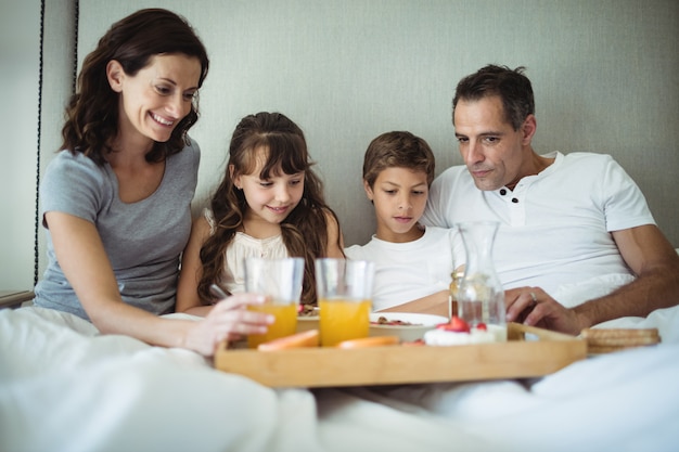 両親とベッドで朝食を持っている子供たち