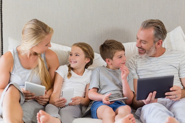 Photo parents and kids interacting while using digital tablet on bed