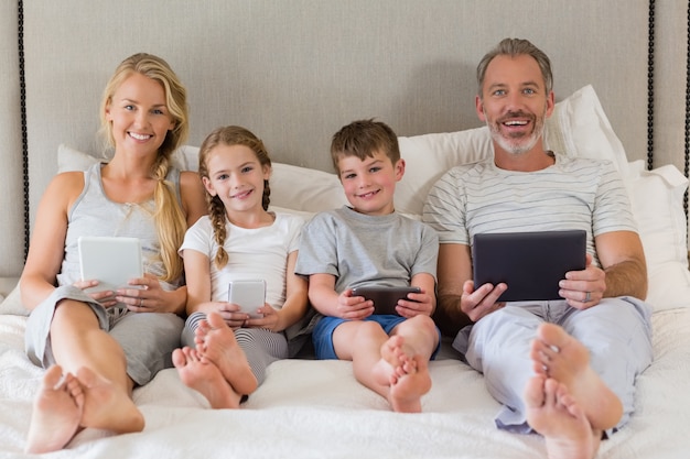 Photo parents and kids using mobile phone and digital tablet on bed