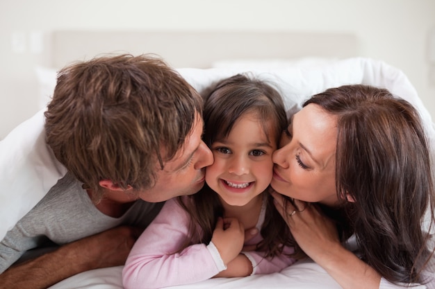 Parents kissing their daughter