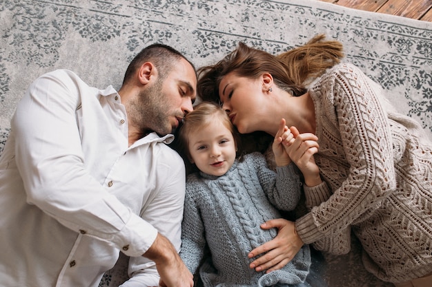 집에서 바닥에 누워있는 작은 딸을 키스하는 부모.