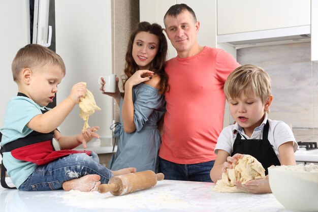 I genitori guardano i loro figli piccoli, che impastano la pasta sul tavolo della cucina