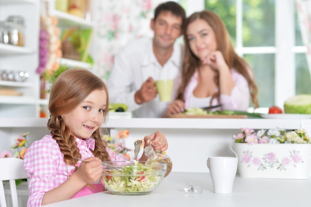 Parents looking how their cute little daughter preparing salad