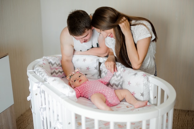 Parents looking on their little daughter in the pink romper in the bed