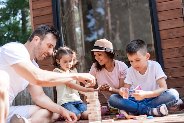 Parents play with their children, having fun playing in Jenga, during the perfect summer vacation out of town. Mom communicates with daughter while playing