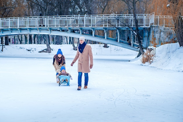 사진 부모는 딸을 썰매에 타고 다리를 배경으로 얼어 붙은 호수를 즐깁니다.