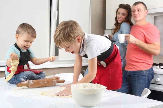 I genitori vedono i loro figli piccoli, che impastano la pasta sul tavolo della cucina